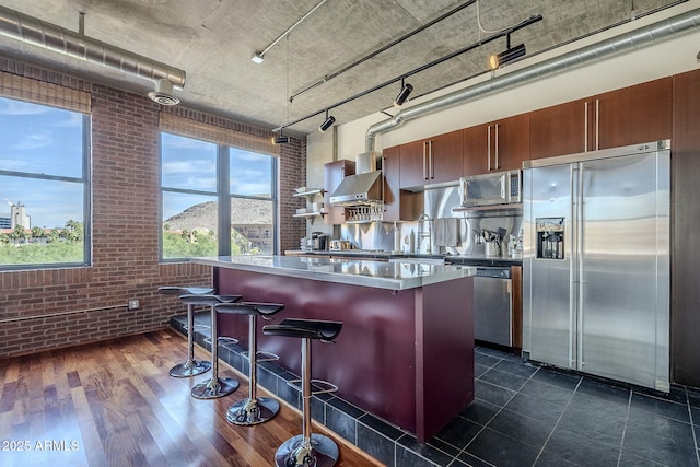 kitchen featuring brick wall, a sink, a kitchen bar, a kitchen island, and appliances with stainless steel finishes