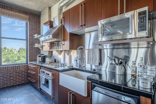 kitchen featuring brick wall, a sink, backsplash, dark countertops, and stainless steel appliances