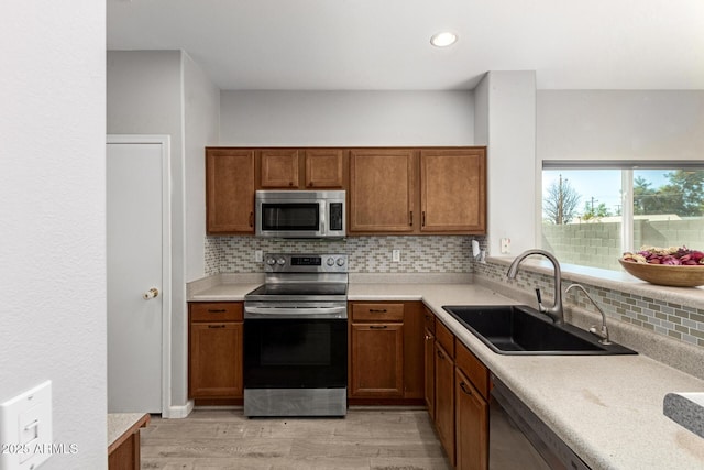 kitchen featuring stainless steel appliances, decorative backsplash, light hardwood / wood-style floors, and sink