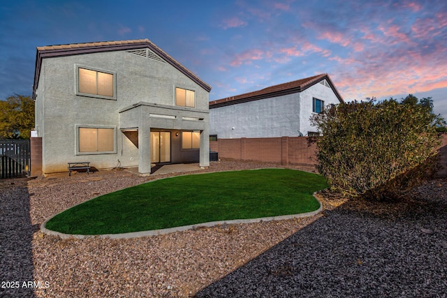 back house at dusk featuring a lawn and a patio