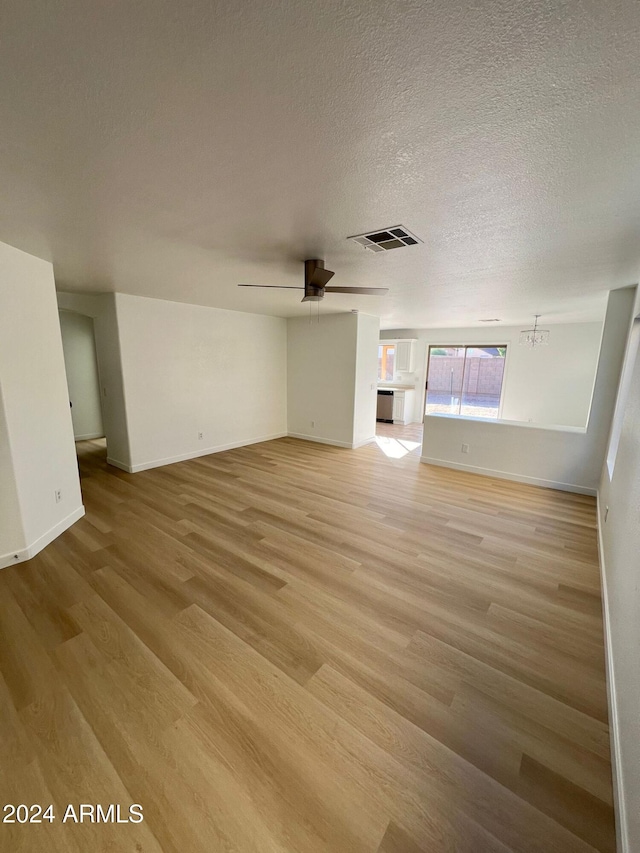 unfurnished living room with ceiling fan with notable chandelier, light hardwood / wood-style floors, and a textured ceiling