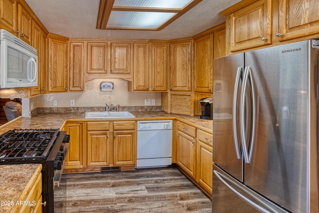 kitchen featuring white appliances, a sink, wood finished floors, and a textured ceiling
