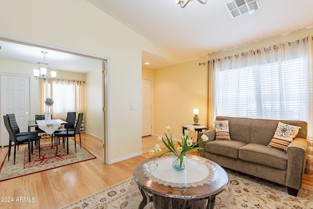 living room with a wealth of natural light, a notable chandelier, light hardwood / wood-style floors, and vaulted ceiling