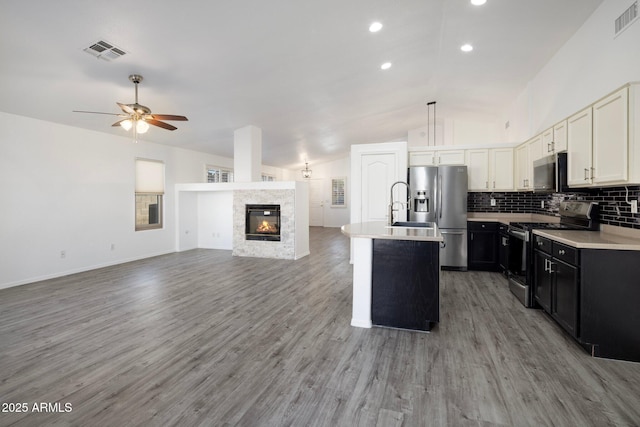 kitchen with stainless steel appliances, white cabinets, lofted ceiling, an island with sink, and backsplash