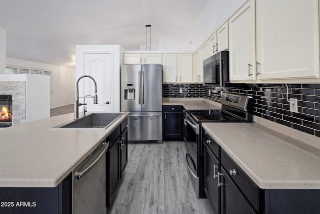 kitchen with decorative light fixtures, stainless steel appliances, an island with sink, light hardwood / wood-style floors, and sink