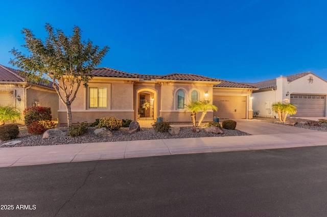 mediterranean / spanish-style house with driveway, a tiled roof, an attached garage, and stucco siding