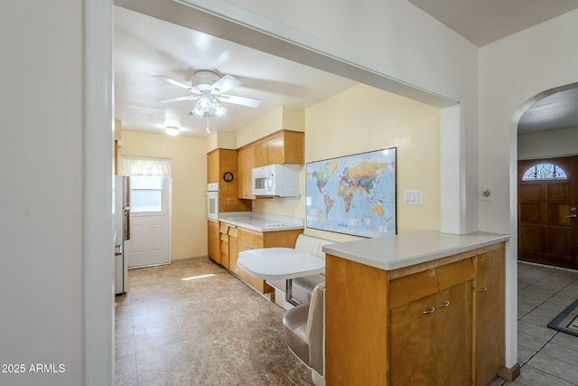 kitchen featuring white appliances, arched walkways, a ceiling fan, a peninsula, and light countertops