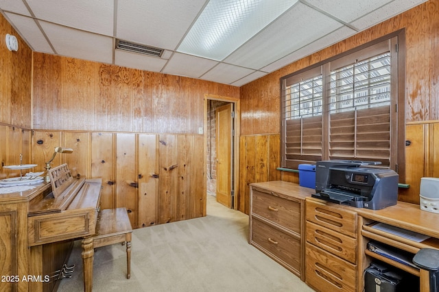 office space with wood walls, visible vents, a drop ceiling, and light colored carpet