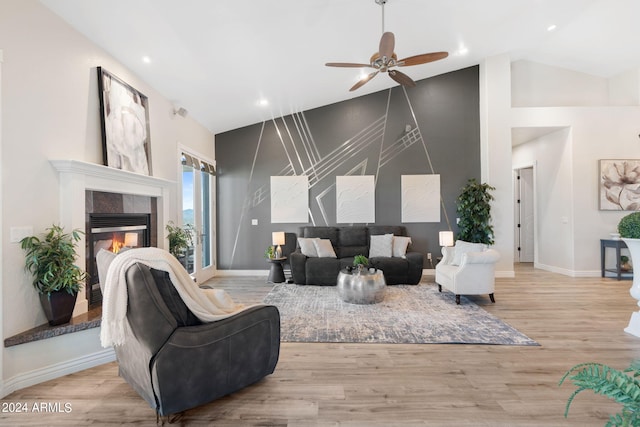 living room with ceiling fan, lofted ceiling, a tiled fireplace, and light hardwood / wood-style flooring