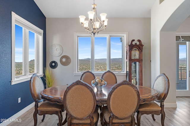 dining room with light hardwood / wood-style flooring, a mountain view, a notable chandelier, and a healthy amount of sunlight