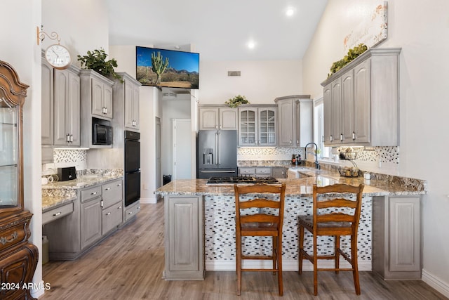 kitchen with kitchen peninsula, light hardwood / wood-style flooring, black appliances, gray cabinets, and decorative backsplash