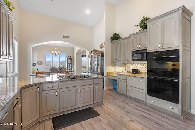 kitchen featuring light hardwood / wood-style floors, high vaulted ceiling, light stone countertops, black appliances, and a notable chandelier