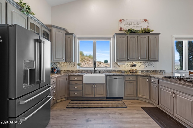 kitchen with tasteful backsplash, stainless steel appliances, light wood-type flooring, lofted ceiling, and sink