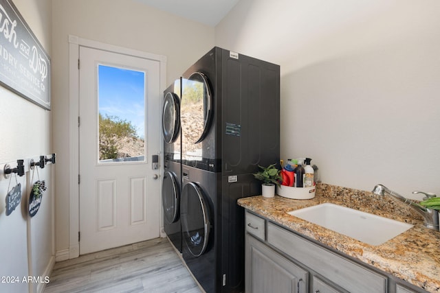 laundry room with stacked washer / dryer, light hardwood / wood-style floors, sink, and cabinets