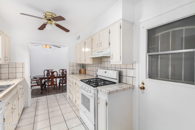 kitchen featuring tile counters, light tile patterned flooring, backsplash, white range with gas cooktop, and white cabinets