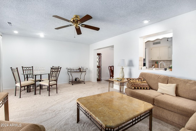 living room with a textured ceiling, light colored carpet, and ceiling fan