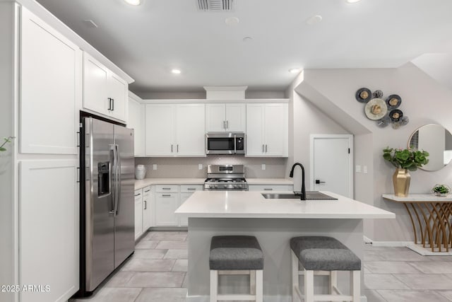 kitchen with appliances with stainless steel finishes, a kitchen breakfast bar, light countertops, white cabinetry, and a sink