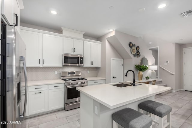 kitchen with light countertops, appliances with stainless steel finishes, a sink, and a center island with sink