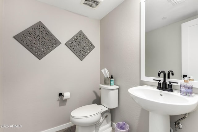 half bath featuring toilet, a sink, visible vents, and baseboards