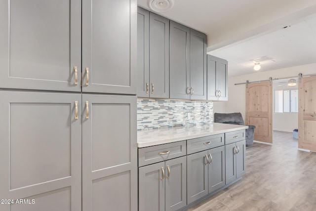 kitchen with gray cabinets, a barn door, light hardwood / wood-style floors, and backsplash