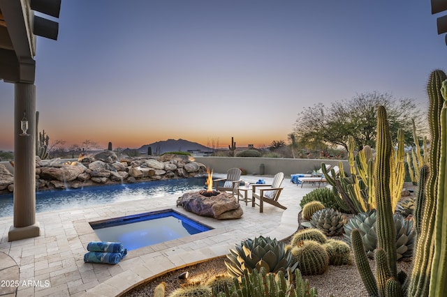 pool at dusk with an outdoor fire pit and a patio