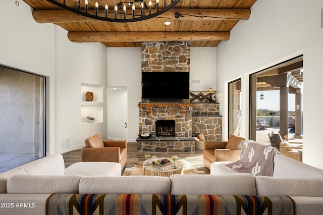 living room with wood finished floors, visible vents, beam ceiling, a stone fireplace, and wooden ceiling