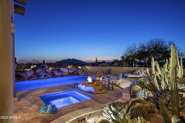 pool at dusk featuring an in ground hot tub, an outdoor fire pit, and a patio