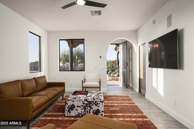 living room with light wood finished floors, visible vents, baseboards, ceiling fan, and arched walkways