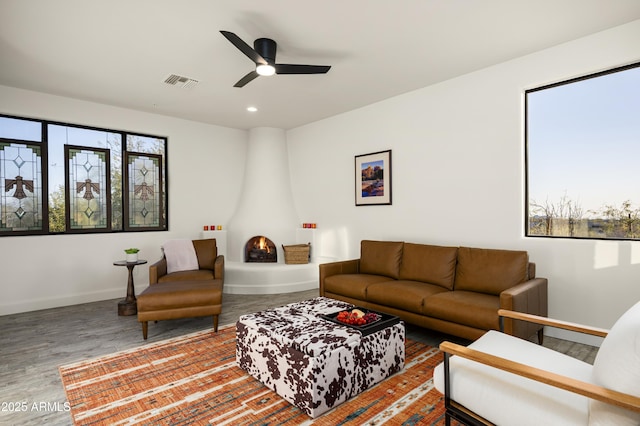 living area with baseboards, wood finished floors, visible vents, and ceiling fan