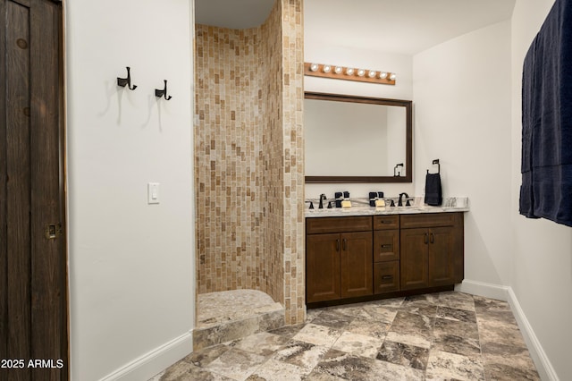 bathroom with a sink, double vanity, baseboards, and tiled shower