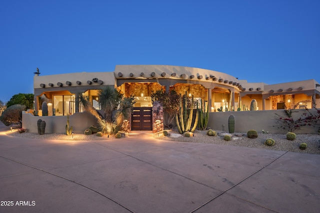 pueblo revival-style home with curved driveway, a fenced front yard, and stucco siding