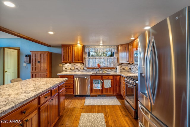 kitchen with light wood-type flooring, a sink, decorative backsplash, appliances with stainless steel finishes, and brown cabinets