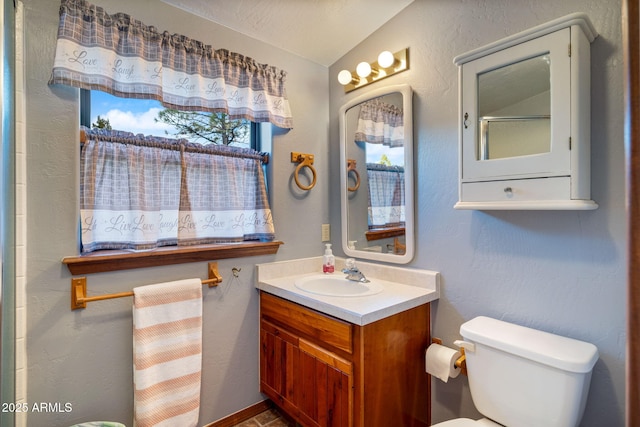 bathroom featuring lofted ceiling, toilet, vanity, and a textured wall