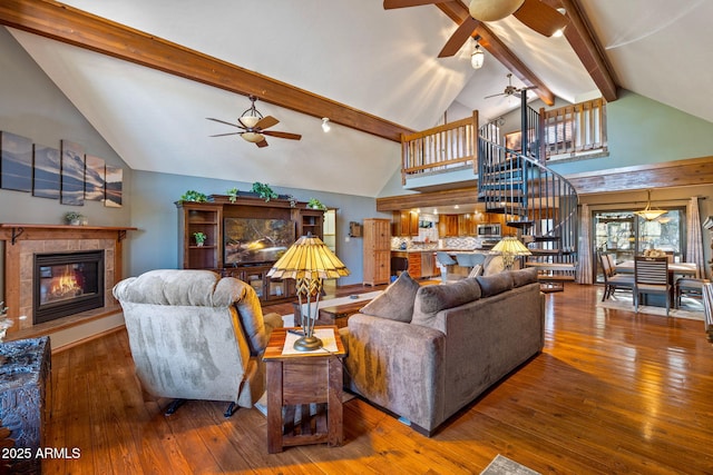 living area with a tiled fireplace, stairway, vaulted ceiling with beams, and wood-type flooring