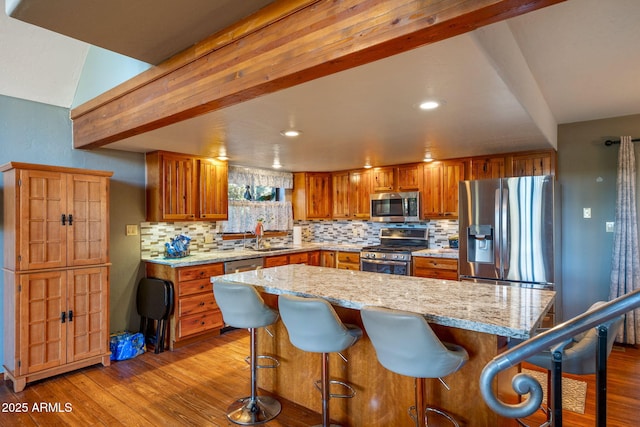 kitchen with wood finished floors, brown cabinetry, stainless steel appliances, beamed ceiling, and backsplash