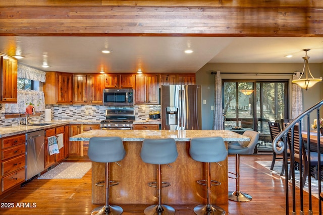 kitchen featuring brown cabinets, a sink, hardwood / wood-style floors, appliances with stainless steel finishes, and decorative backsplash