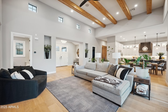 living room featuring beamed ceiling, light hardwood / wood-style flooring, and a high ceiling