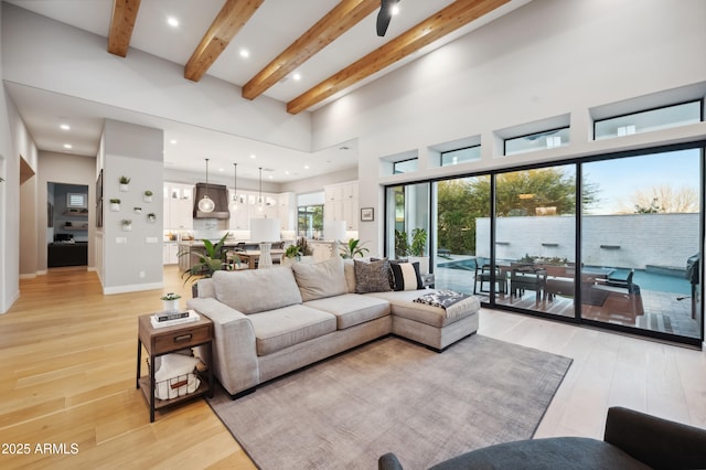 living room with beamed ceiling, a high ceiling, and light wood-type flooring