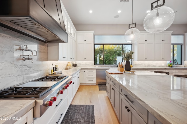 kitchen featuring premium range hood, white cabinetry, decorative light fixtures, and light stone countertops