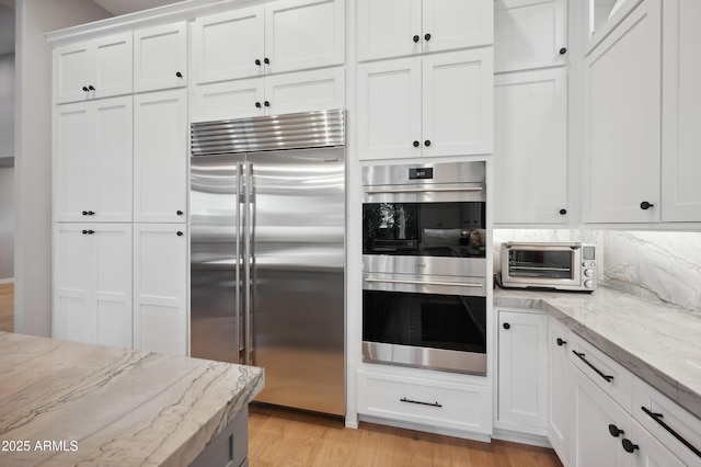 kitchen with light stone counters, tasteful backsplash, white cabinets, and appliances with stainless steel finishes