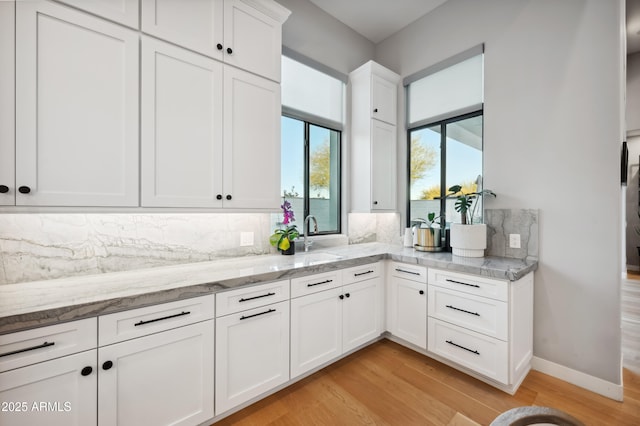 kitchen with light stone counters, sink, tasteful backsplash, and white cabinets