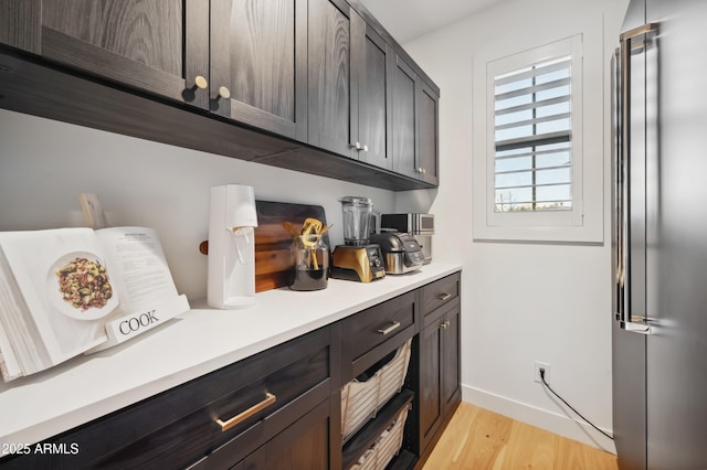 bar featuring high end refrigerator, dark brown cabinets, and light wood-type flooring