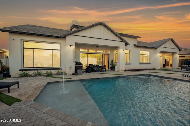 back house at dusk with a patio area, pool water feature, and ceiling fan