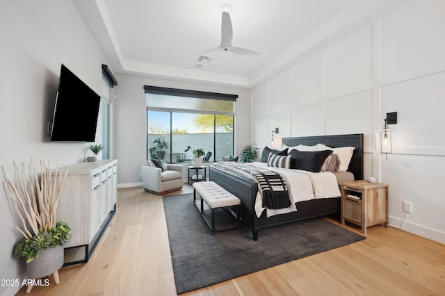 bedroom with a tray ceiling, ceiling fan, and light hardwood / wood-style flooring