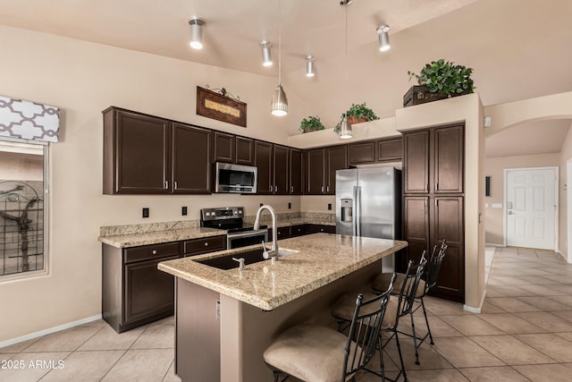 kitchen with a sink, arched walkways, dark brown cabinetry, appliances with stainless steel finishes, and light tile patterned flooring