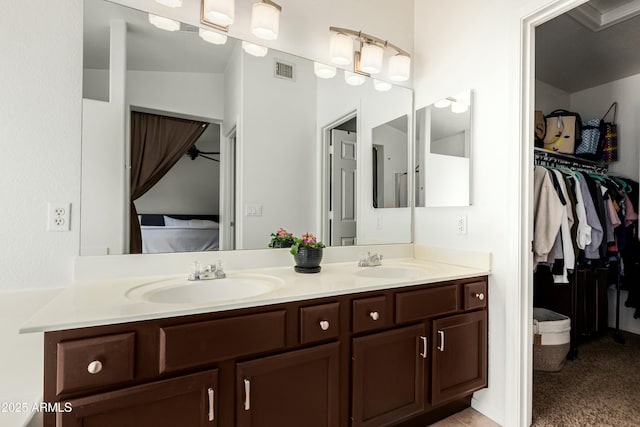 ensuite bathroom with double vanity, visible vents, a walk in closet, and a sink