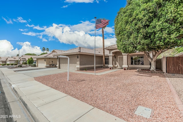 view of front of property featuring an attached garage, fence, a tile roof, stucco siding, and driveway