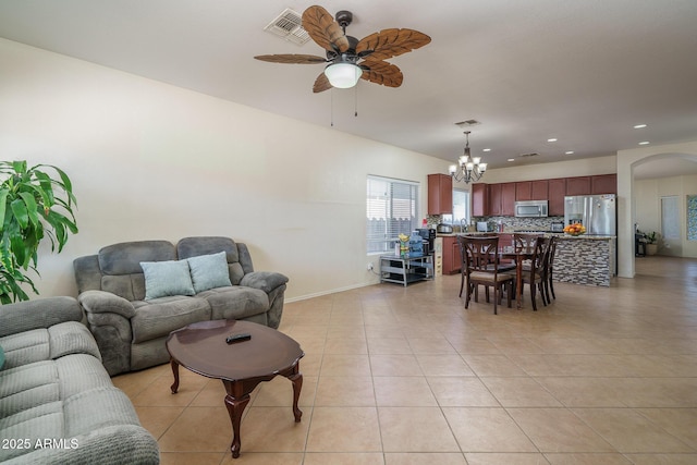 living area featuring light tile patterned flooring, arched walkways, visible vents, and ceiling fan with notable chandelier