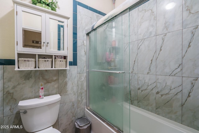 bathroom with bath / shower combo with glass door, toilet, and tile walls