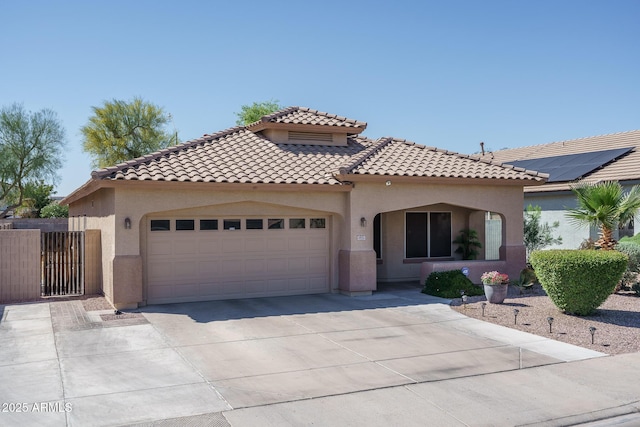 mediterranean / spanish home featuring a tile roof, driveway, stucco siding, fence, and an attached garage